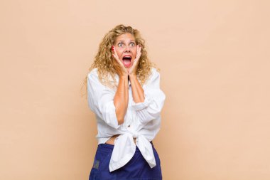 Orta yaşlı bir kadın, mutlu, heyecanlı ve şaşırmış hissediyor, iki eli yüzü yana bakıyor.