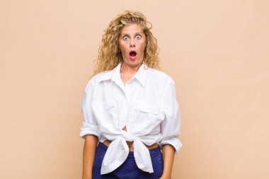 Orta yaşlı kadın şaşkın, mutlu, şaşkın ve şaşırmış hissediyor, ağzı açık bir şekilde yana bakıyor.