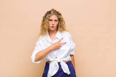 Orta yaşlı bir kadın mutlu, pozitif ve başarılı hissediyor, göğsünde el yapımı V ile, zafer ya da barış gösteriyor.