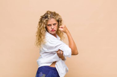 Orta yaşlı bir kadın kendini mutlu, tatmin olmuş ve güçlü hissediyor, kaslı ve formda, spor salonundan sonra güçlü görünüyor.