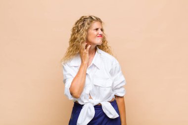 Orta yaşlı bir kadın stresli, hayal kırıklığına uğramış ve yorgun, endişeli ve sorunlu bir bakışla boynunu ovalıyor.