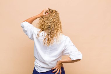 Orta yaşlı bir kadın bilgisiz ve kafası karışık, bir çözüm düşünüyor, eli kalçasında, diğeri kafasında, dikiz aynasından.