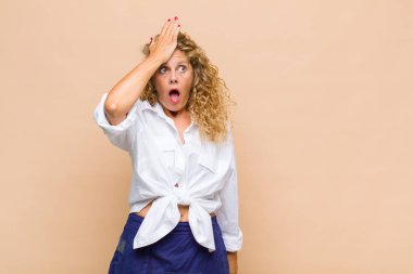 Middle age woman raising palm to forehead thinking oops, after making a stupid mistake or remembering, feeling dumb