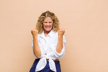 Orta yaşlı bir kadın sinirli bir ifadeyle ya da yumruklarıyla başarıyı kutlarken agresif bir şekilde bağırıyor.