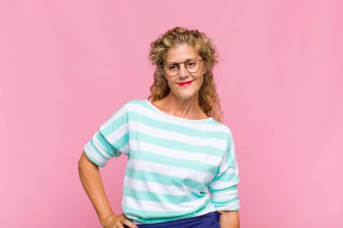 Orta yaşlı bir kadın mutlu bir şekilde gülümsüyor. Kendine güvenen, olumlu, gururlu ve arkadaş canlısı bir tavırla.