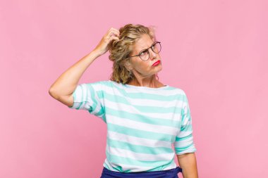 Orta yaşlı kadın şaşkın ve şaşkın hissediyor, kafasını kaşıyor ve yan tarafa bakıyor.