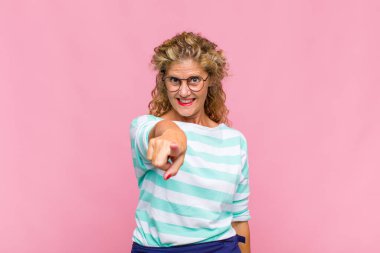 Orta yaşlı bir kadın kameraya bakıyor, kendinden emin, arkadaş canlısı bir gülümsemeyle, seni seçiyor.