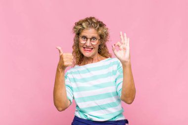 Orta yaşlı bir kadın mutlu, şaşkın, tatmin olmuş ve şaşırmış hissediyor, iyi görünüyor ve el kol hareketleri yapıyor, gülümsüyor.