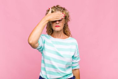 Orta yaşlı bir kadın tek eliyle gözlerini kapatıyor korkmuş ya da endişeli hissediyor, merak ediyor ya da körü körüne bir sürpriz bekliyor.