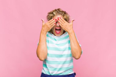 Orta yaşlı bir kadın gülümsüyor ve mutlu hissediyor, iki eliyle gözlerini kapatıyor ve inanılmaz bir sürpriz bekliyor.