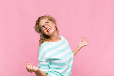 Orta yaşlı kadın gülümsüyor, kaygısız hissediyor, rahat ve mutlu, dans ediyor ve müzik dinliyor, bir partide eğleniyor.