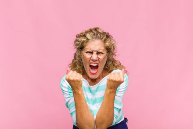 Orta yaşlı bir kadın sinirli, sinirli, kızgın bakışlar ve sıkı yumruklarla bağırıyor. Öfkeli hissediyor.