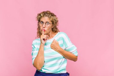 Orta yaşlı kadın ciddi görünüyor ve parmaklarını dudaklarına bastırıp sessizlik ya da sessizlik talep ediyor, sır saklıyor.