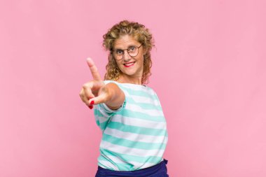 Orta yaşlı bir kadın gururla gülümsüyor ve gururla bir numaralı pozunu veriyor, kendini lider gibi hissediyor.