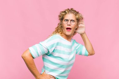 Orta yaşlı kadın gülümsüyor, tuhaf bir şekilde yan tarafa bakıyor, dedikoduları dinlemeye ya da bir sırrı duymaya çalışıyor.