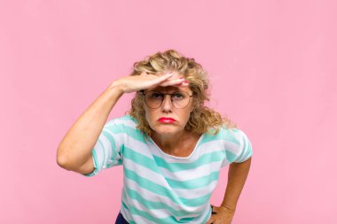 Orta yaşlı kadın şaşkınlık ve şaşkınlık içinde bakıyor. Alnı açık, uzaklara bakıyor, izliyor ya da arıyor.