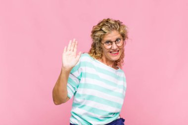 Orta yaşlı bir kadın mutlu ve neşeli bir şekilde gülümsüyor, el sallıyor, sizi selamlıyor ve selamlıyor, ya da veda ediyor.