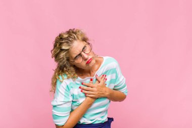 Orta yaşlı bir kadın üzgün, yaralı ve kalbi kırık görünüyor, iki elini de kalbe yakın tutuyor, ağlıyor ve bunalımda.