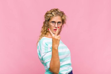 Orta yaşlı bir kadın gülümsüyor ve arkadaş canlısı görünüyor. İki ya da iki numarayı gösteriyor. Elleri önde, geriye doğru sayıyor.