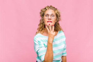 Orta yaşlı bir kadın gülümsüyor ve arkadaş canlısı görünüyor. Üç ya da üç numarayı gösteriyor. Elleri önde, geri sayıyor.