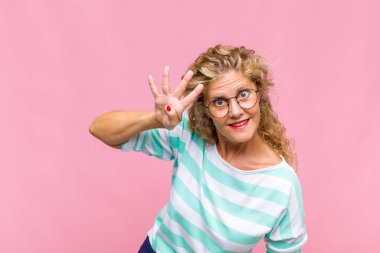 Orta yaşlı bir kadın gülümsüyor ve arkadaş canlısı görünüyor. Elleri önde, geriye doğru sayıyor.