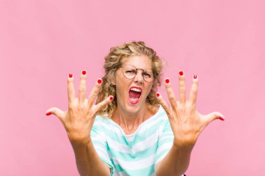 Orta yaşlı bir kadın gülümsüyor ve arkadaş canlısı görünüyor, onuncu veya onuncu numarayı gösteriyor, eli önde, geriye doğru sayıyor.