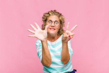 Orta yaşlı bir kadın gülümsüyor ve dost canlısı görünüyor, 7 ya da 7 numarayı gösteriyor, eli önde, geriye doğru sayıyor.