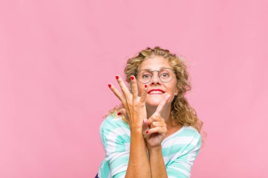 Orta yaşlı bir kadın gülümsüyor ve arkadaş canlısı görünüyor, altı ya da altıncı numarayı gösteriyor, eli önde, geriye doğru sayıyor.