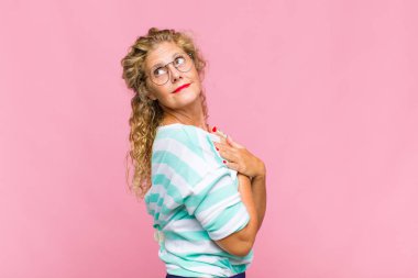 Orta yaşlı bir kadın neşeyle gülümsüyor, mutlu, tatmin olmuş ve rahatlamış hissediyor, kollarını kavuşturup yan tarafa bakıyor.