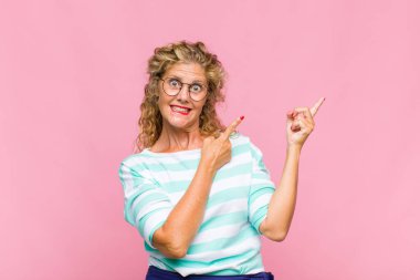 Orta yaşlı kadın mutlu bir şekilde gülümsüyor ve her iki elinde fotokopi uzayında nesne gösteriyor.