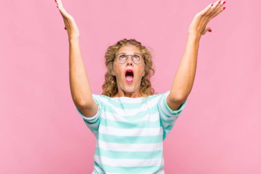 Orta yaşlı bir kadın kendini mutlu, şaşkın, şanslı ve şaşırmış hissediyor. Zaferi iki eli havada kutluyor.