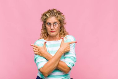 Orta yaşlı kadın şaşkın ve şaşkın görünüyor, güvensiz ve şüpheyle zıt yönleri işaret ediyor.