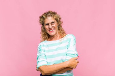 Orta yaşlı bir kadın mutlu, gururlu ve tatmin olmuş görünüyor. Kollarını kavuşturup gülümsüyor.