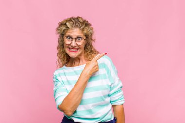 Orta yaşlı bir kadın heyecanlı ve şaşırmış görünüyor. Kenarlarını ve yukarısını göstererek boşluğu kopyalıyor.