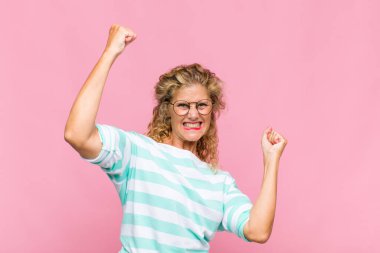 Orta yaşlı bir kadın muzaffer bir şekilde bağırıyor, heyecanlı, mutlu ve şaşırmış görünüyor, kutlama yapıyor.