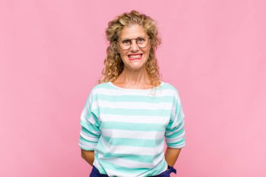 Orta yaşlı bir kadın mutlu ve şapşal görünüyor. Geniş, eğlenceli, kaçık bir gülüşü ve gözleri var.