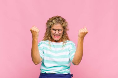 Orta yaşlı bir kadın mutlu, şaşırmış ve gururlu hissediyor, bağırıyor ve başarıyı büyük bir gülümsemeyle kutluyor.