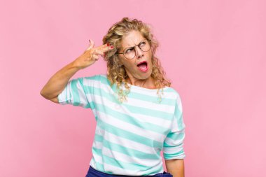 Orta yaşlı kadın mutsuz ve stresli görünüyor, intihar jesti elle silah işareti yapıyor, kafasını işaret ediyor.