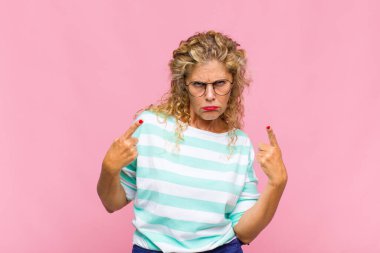 Kötü tavırlı orta yaşlı bir kadın gururlu ve agresif görünüyor, yukarıyı gösteriyor ya da elleriyle alay işareti yapıyor.