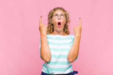 Orta yaşlı bir kadın şaşırmış ve ağzı açık bir şekilde şaşkın ve şaşkın bir bakışla yukarı bakıyor.