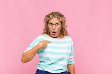 Orta yaşlı kadın şok olmuş ve şaşırmış görünüyor ağzı açık, kendini işaret ediyor.