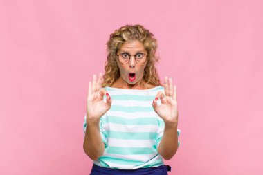 Orta yaşlı kadın şok olmuş, şaşırmış ve şaşırmış hissediyor. Onaylıyor. İki eliyle de onay işareti yapıyor.