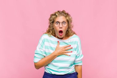 Orta yaşlı bir kadın şaşkın ve şaşırmış hissediyor, gülümsüyor, el ele tutuşuyor, o olmaktan mutlu ya da minnettarlık gösteriyor.