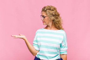 Orta yaşlı bir kadın kendini mutlu hissediyor ve gülümsüyor. Elinde tuttuğu bir nesneye ya da konsepte bakıyor.