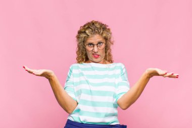 Middle age woman shrugging with a dumb, crazy, confused, puzzled expression, feeling annoyed and clueless