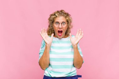 Orta yaşlı bir kadın beklenmedik bir sürpriz yüzünden şaşkın, heyecanlı, gülen, şaşkın ve mutlu hissediyor.