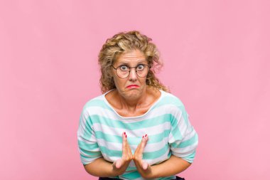 Orta yaşlı bir kadın, şaşkın ve tuhaf bakışlarıyla kendini işaret ediyor. Seçildiğine şaşırmış ve şaşırmış.