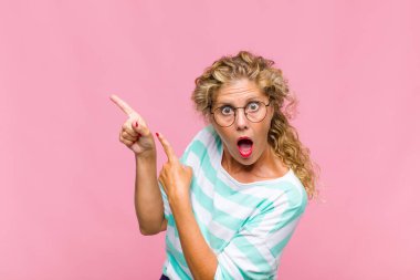 Orta yaşlı bir kadın mutlu ve şaşırmış hissediyor. Şok olmuş bir ifadeyle gülümsüyor ve bir tarafı işaret ediyor.