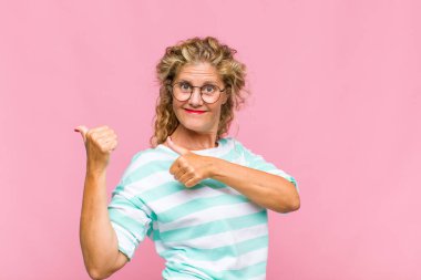 Orta yaşlı kadın neşeli bir şekilde gülümsüyor ve yan taraftaki fotokopi alanını işaret ediyor, mutlu ve tatmin olmuş hissediyor.