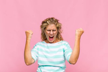 Orta yaşlı bir kadın sinirli bir ifadeyle ya da yumruklarıyla başarıyı kutlarken agresif bir şekilde bağırıyor.